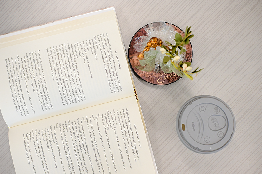 Open book on a table next to a plant and coffee cup