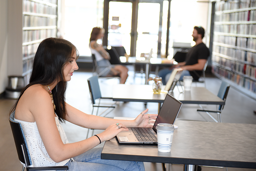 Teen girl sitting at a library table with an open laptop