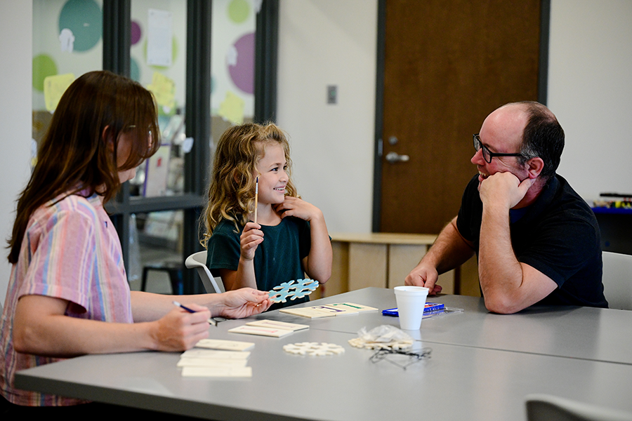 Girl and two adults sitting at a table in the library doing a learning craft