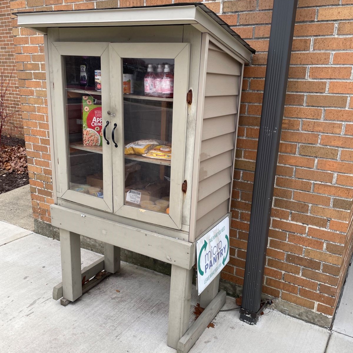 Brown cabinet with glass doors and three shelves stocked with nonperishable food outside of the library building