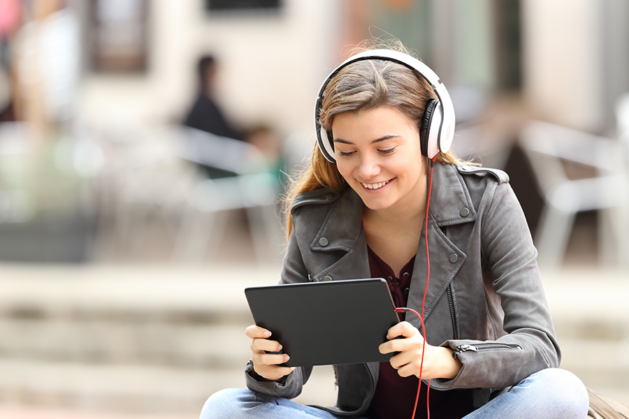 Teen girl with headphones smiling and looking at a tablet