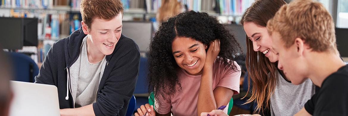 Group of teens, two boys and two girls, sitting at a library table and studying together